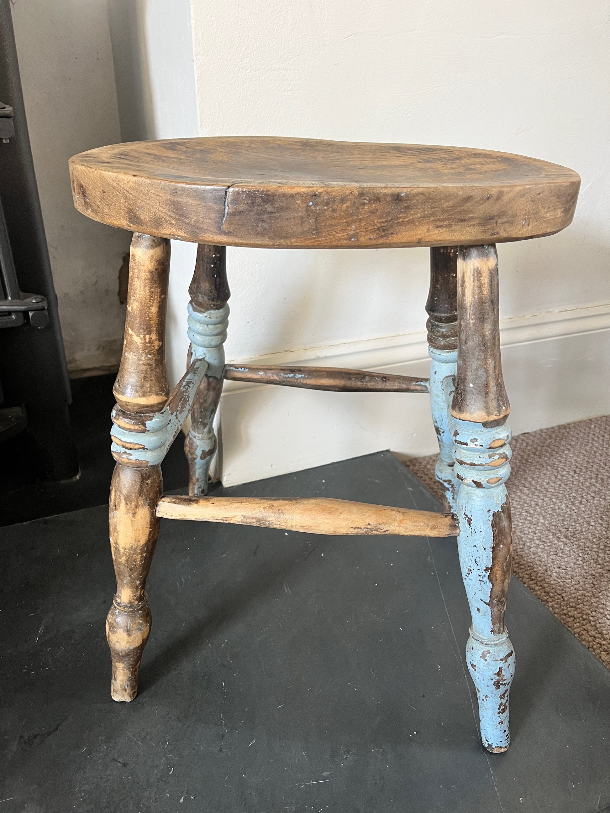A collection of rustic wooden stools, each with a weathered finish in varying shades of brown, blue and yellow, featuring simple, sturdy designs with four legs
