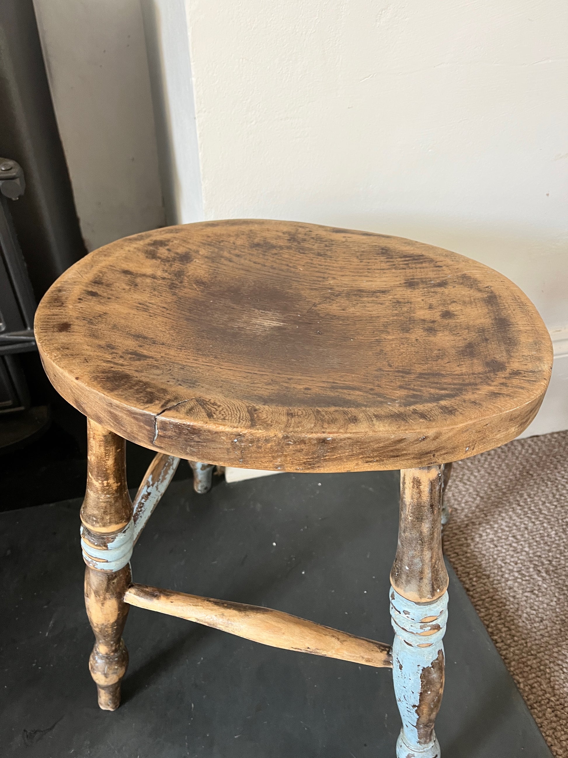 A collection of rustic wooden stools, each with a weathered finish in varying shades of brown, blue and yellow, featuring simple, sturdy designs with four legs