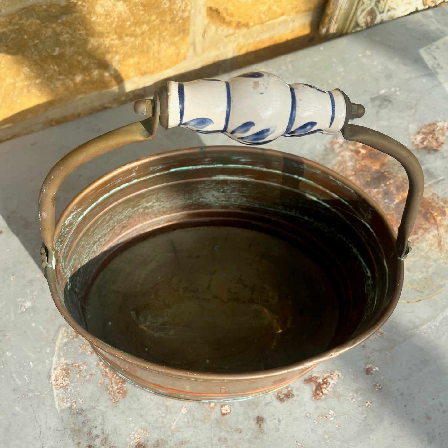 A vintage French copper planter with a glossy finish, featuring a delicate china handle adorned with a blue and white floral pattern.