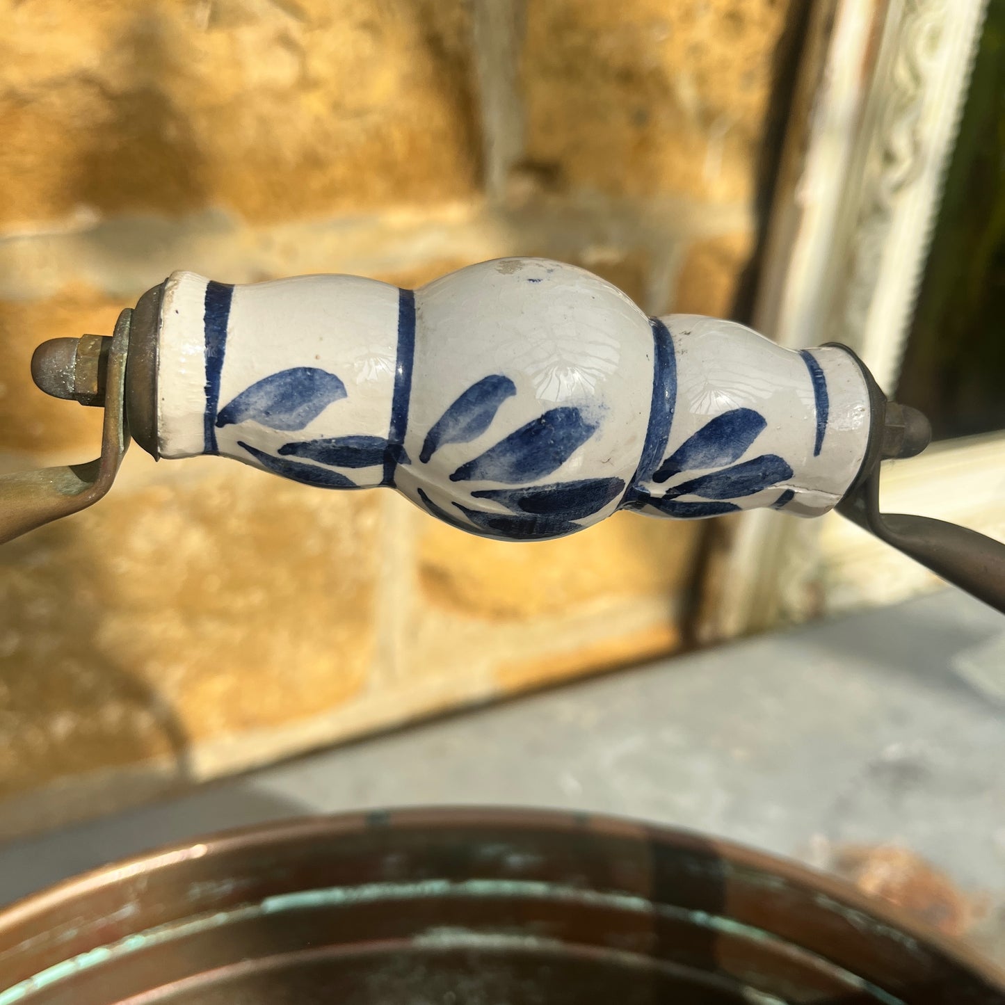 A vintage French copper planter with a glossy finish, featuring a delicate china handle adorned with a blue and white floral pattern.
