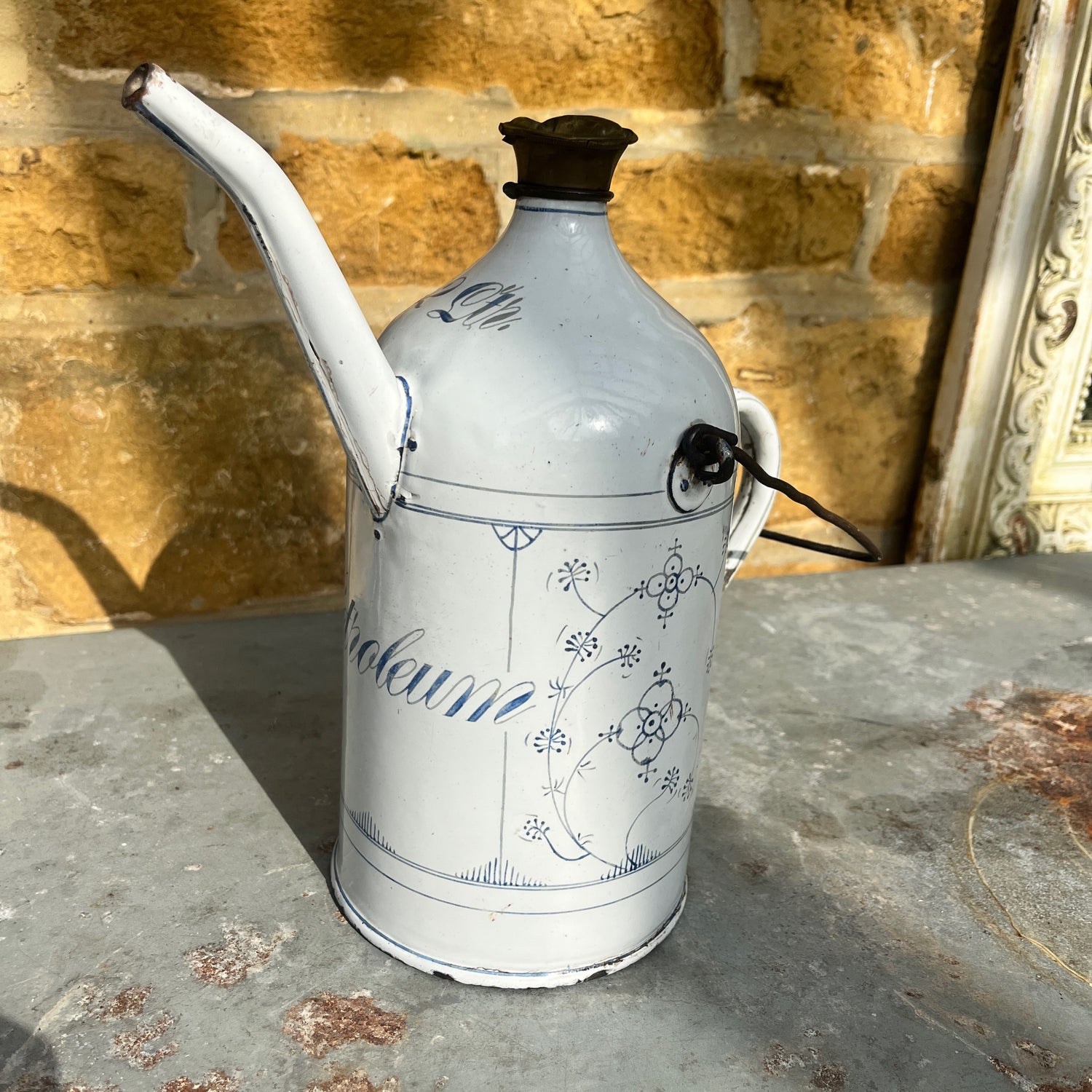 A vintage French enamel petroleum canister with a glossy finish, featuring elegant blue and white detailing in a classic pattern.