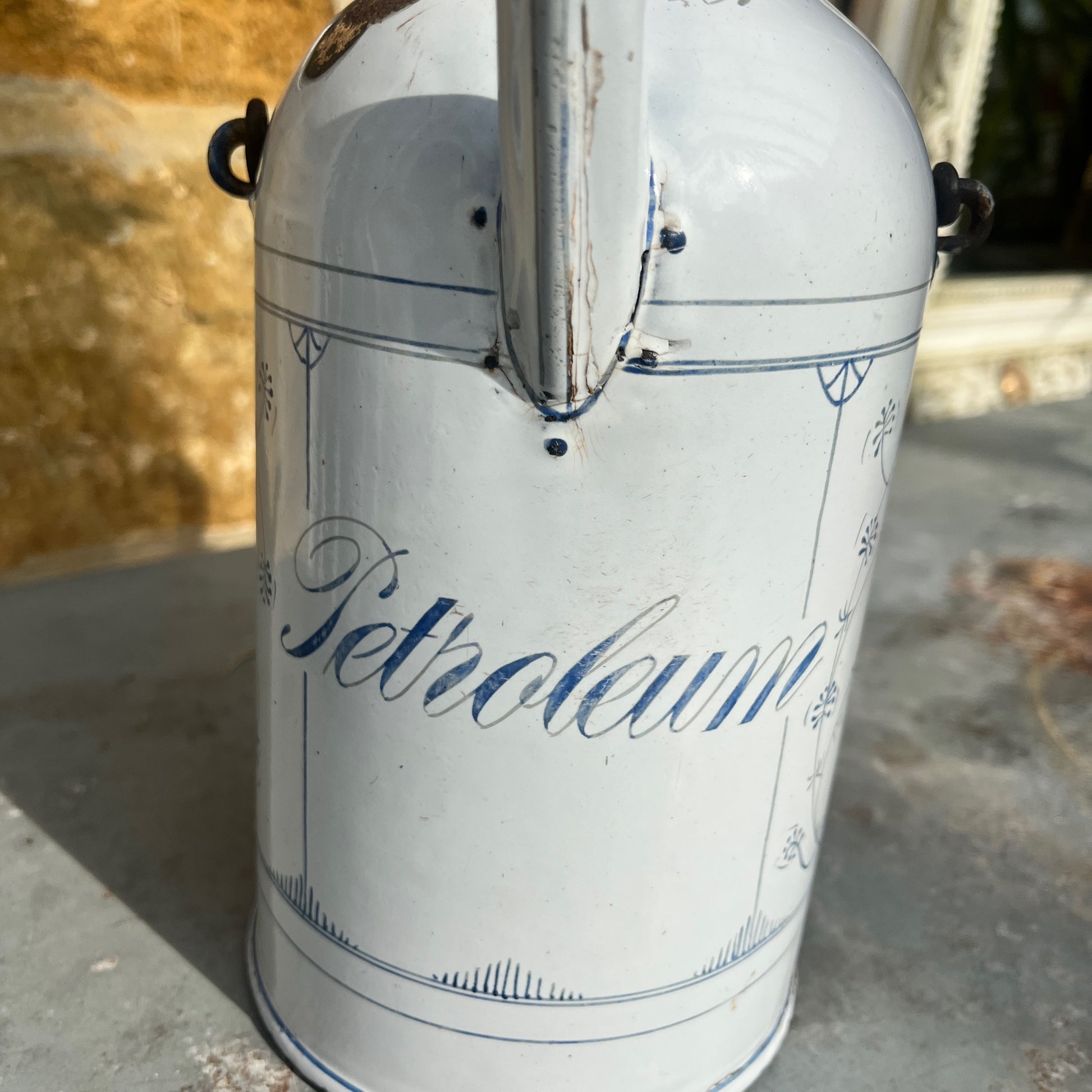 A vintage French enamel petroleum canister with a glossy finish, featuring elegant blue and white detailing in a classic pattern.