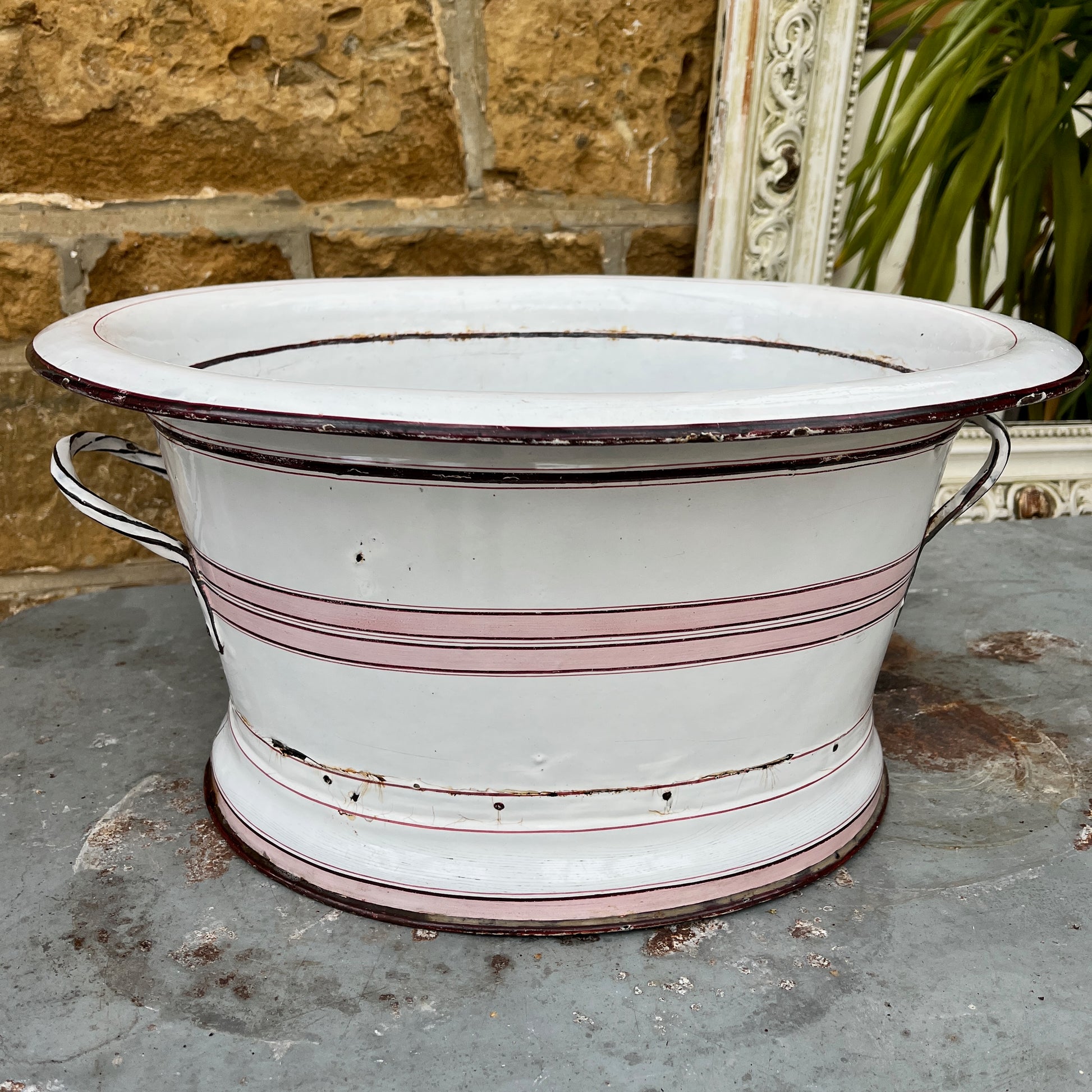 A large vintage French white enamel wash bowl, circa early 20th century, featuring a wide, deep basin. The bowl is adorned with delicate pink stripes,  with a smooth white enamel finish showing minor chips and rust spots, characteristic of its aged, rustic charm.