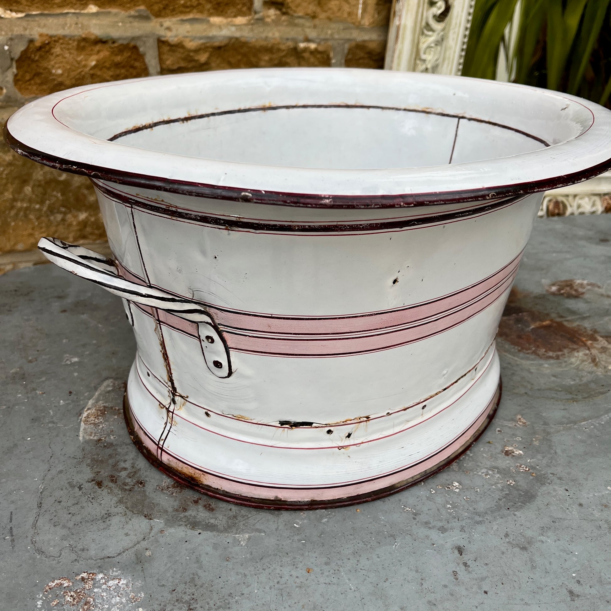 A large vintage French white enamel wash bowl, circa early 20th century, featuring a wide, deep basin. The bowl is adorned with delicate pink stripes,  with a smooth white enamel finish showing minor chips and rust spots, characteristic of its aged, rustic charm.