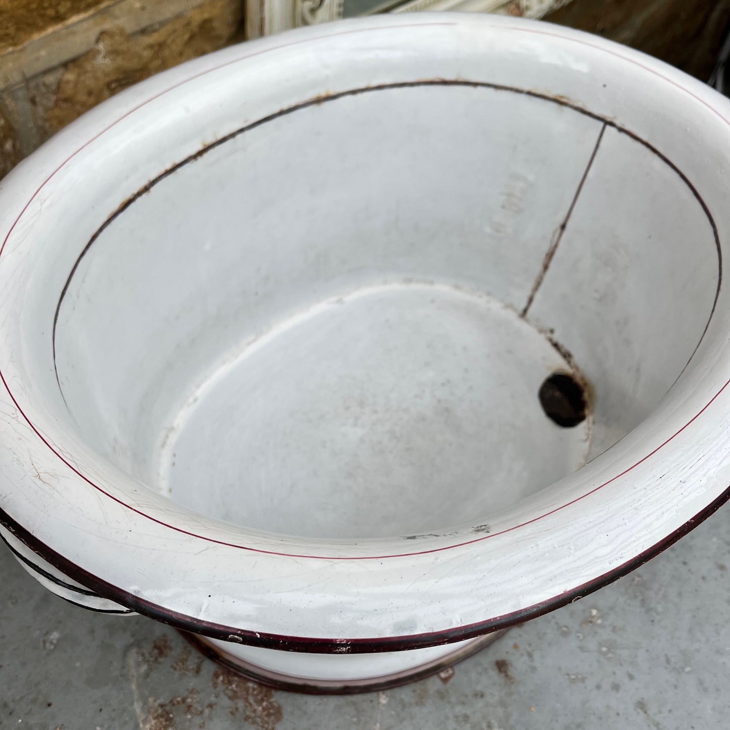 A large vintage French white enamel wash bowl, circa early 20th century, featuring a wide, deep basin. The bowl is adorned with delicate pink stripes,  with a smooth white enamel finish showing minor chips and rust spots, characteristic of its aged, rustic charm.
