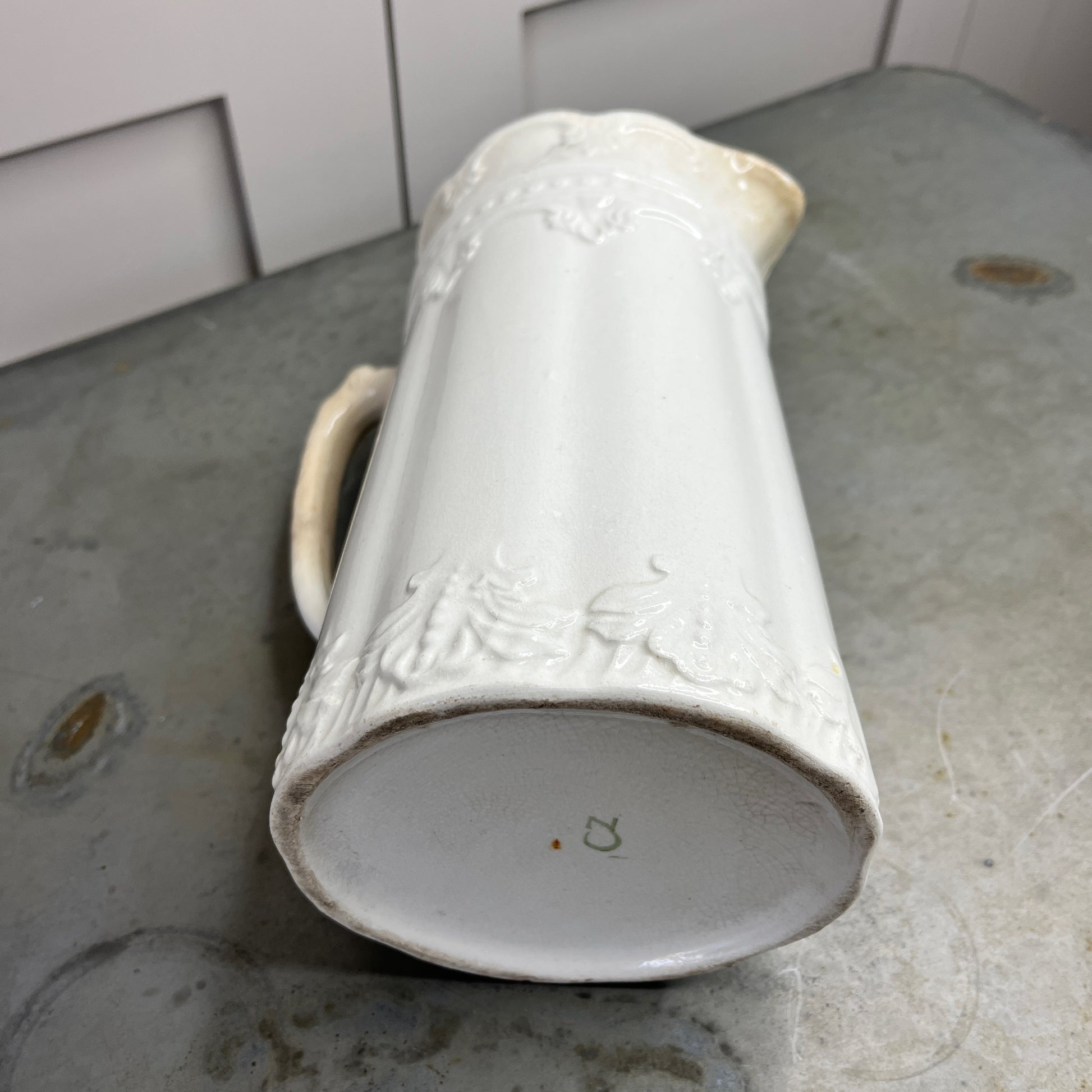 White ceramic pitcher with decorative patterns on a gray surface.