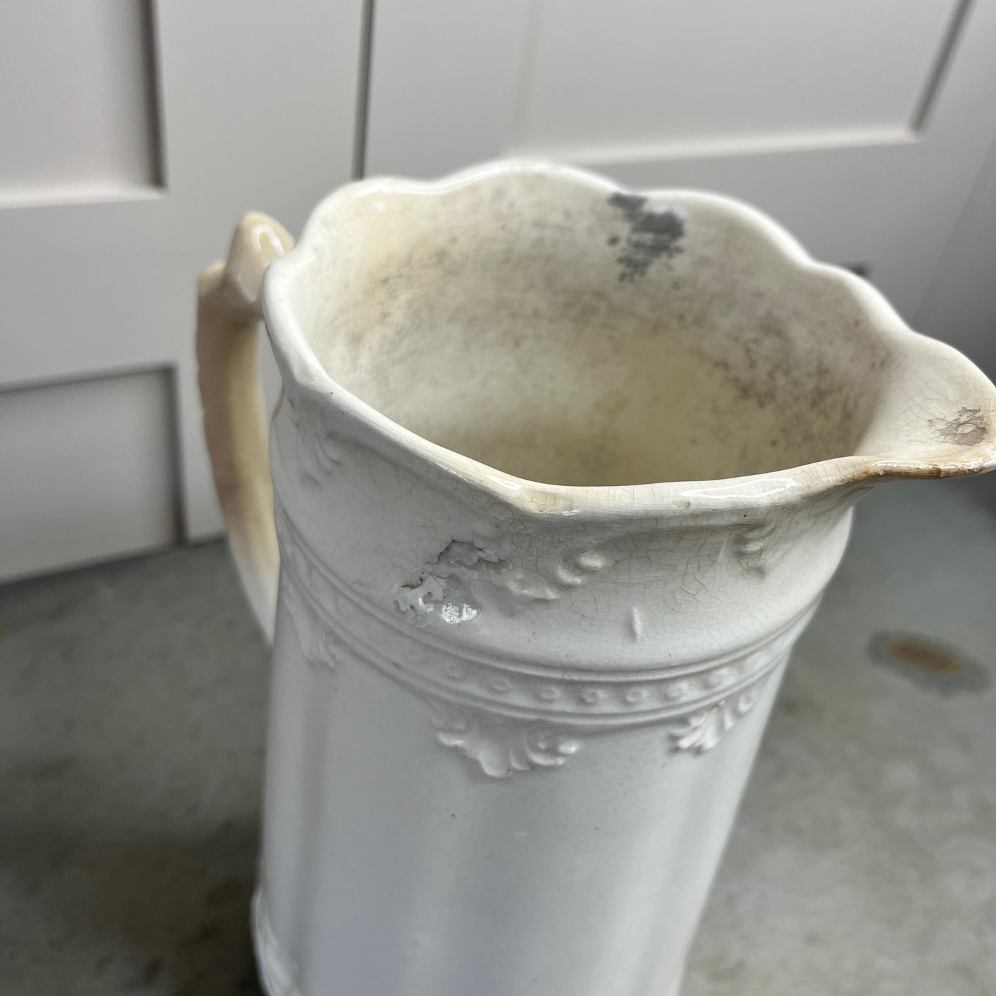 White ceramic pitcher with decorative patterns on a gray surface.