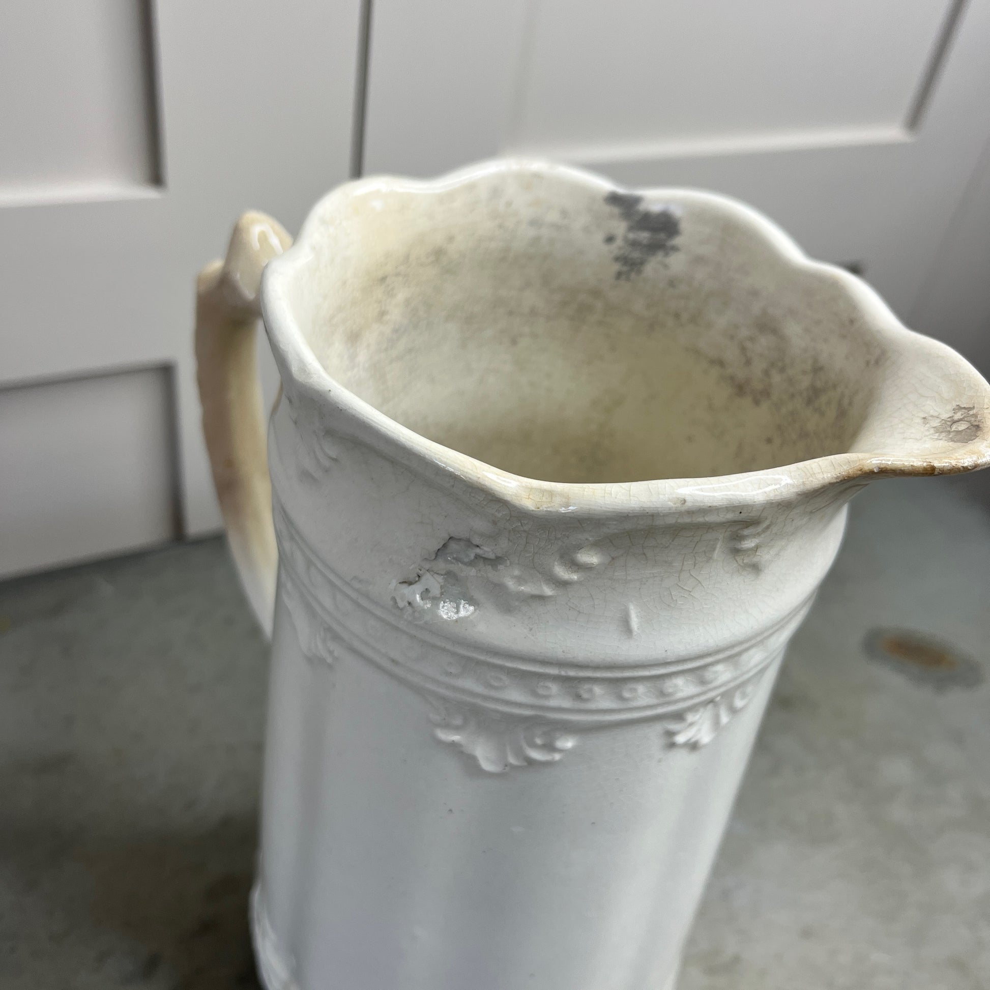 White ceramic pitcher with decorative patterns on a gray surface.