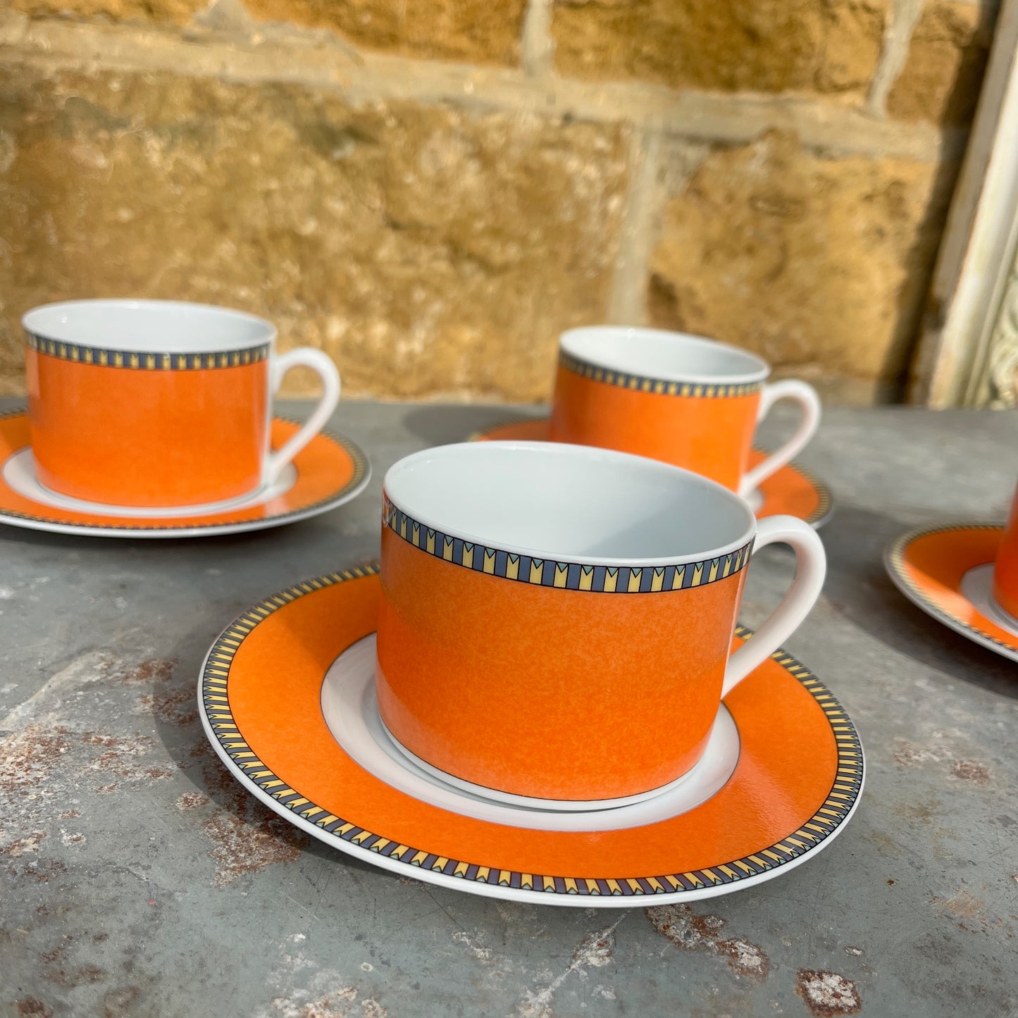 Orange teacups and saucers with decorative rims and white interior.