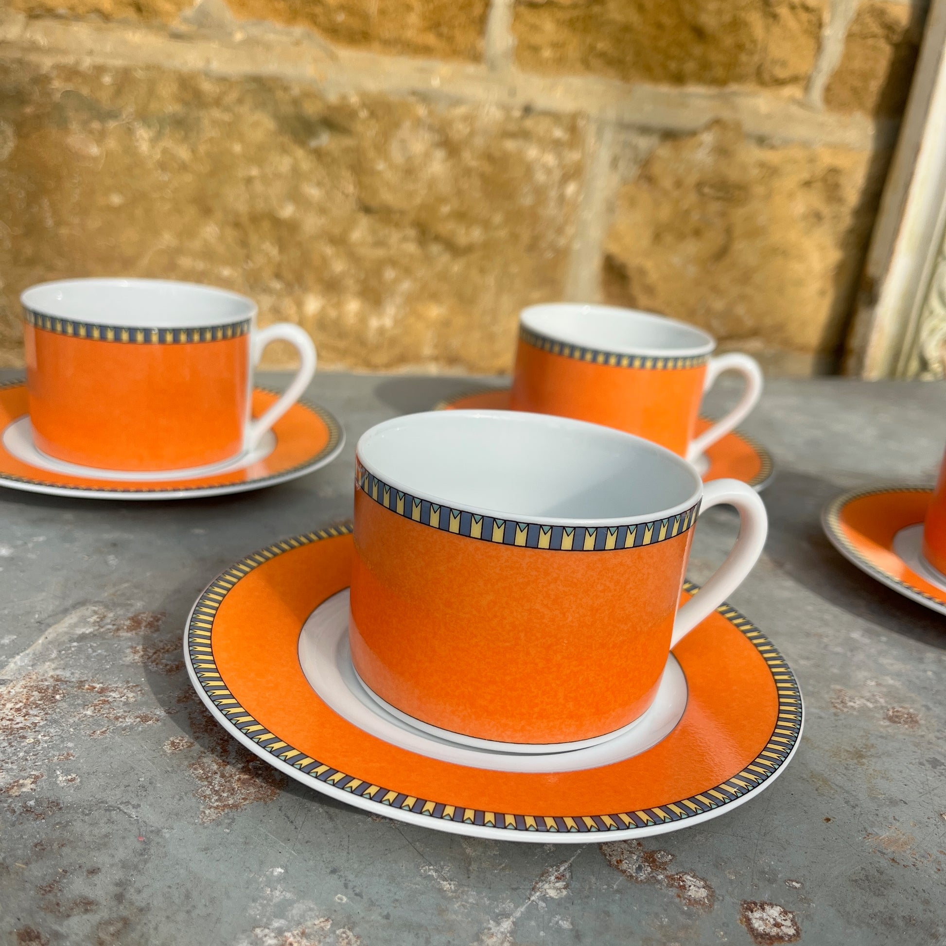 Orange teacups and saucers with decorative rims and white interior.
