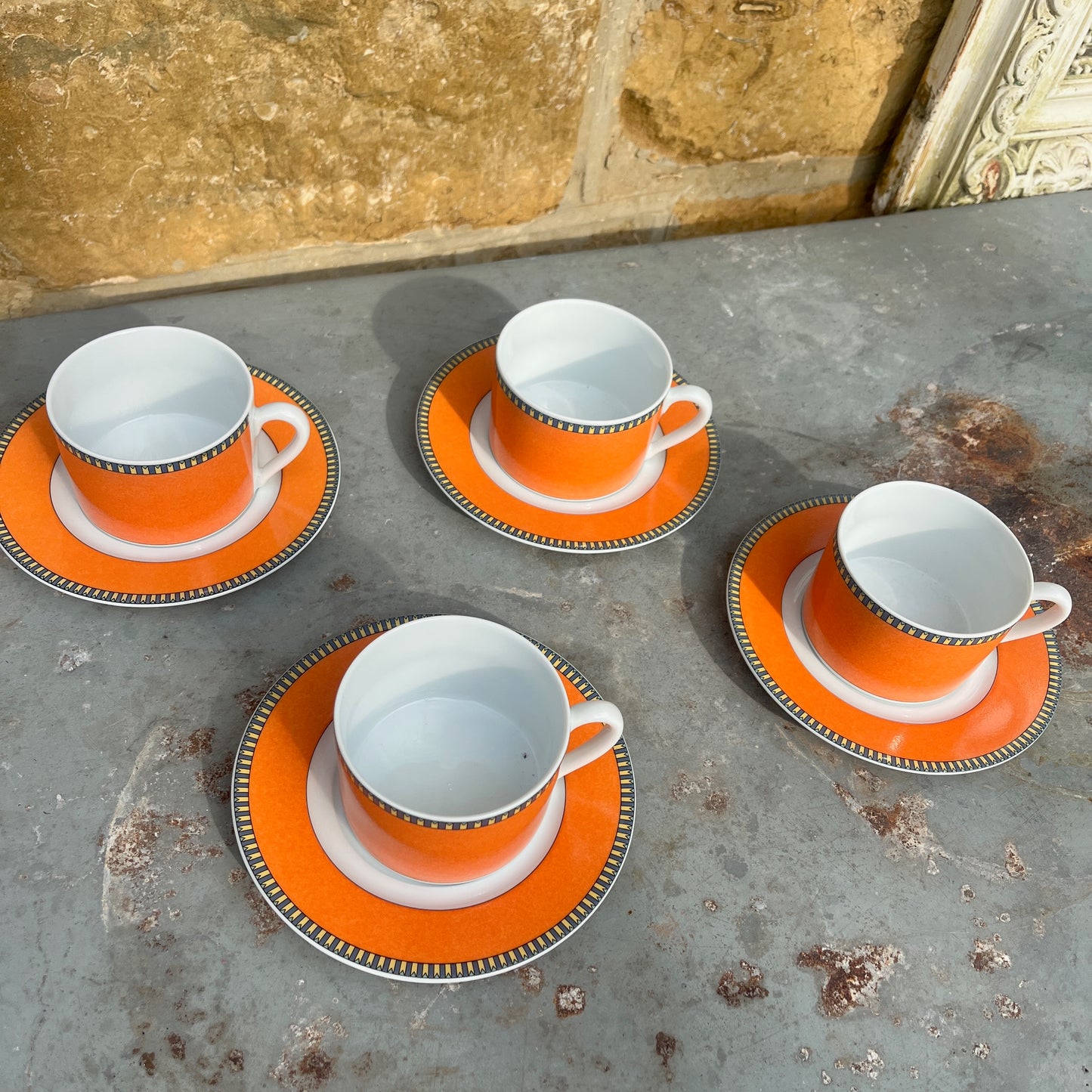 Orange teacups and saucers with decorative rims and white interior.