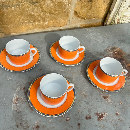 Orange teacups and saucers with decorative rims and white interior.