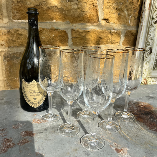 A set of six vintage champagne flutes with elegant gold rims and intricately etched glass, circa mid-20th century. Each flute features delicate floral or geometric etchings on the bowl, complemented by a fine gold band around the rim.