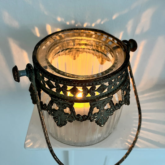 Small glass tea light holder with decorative metal top and handle.