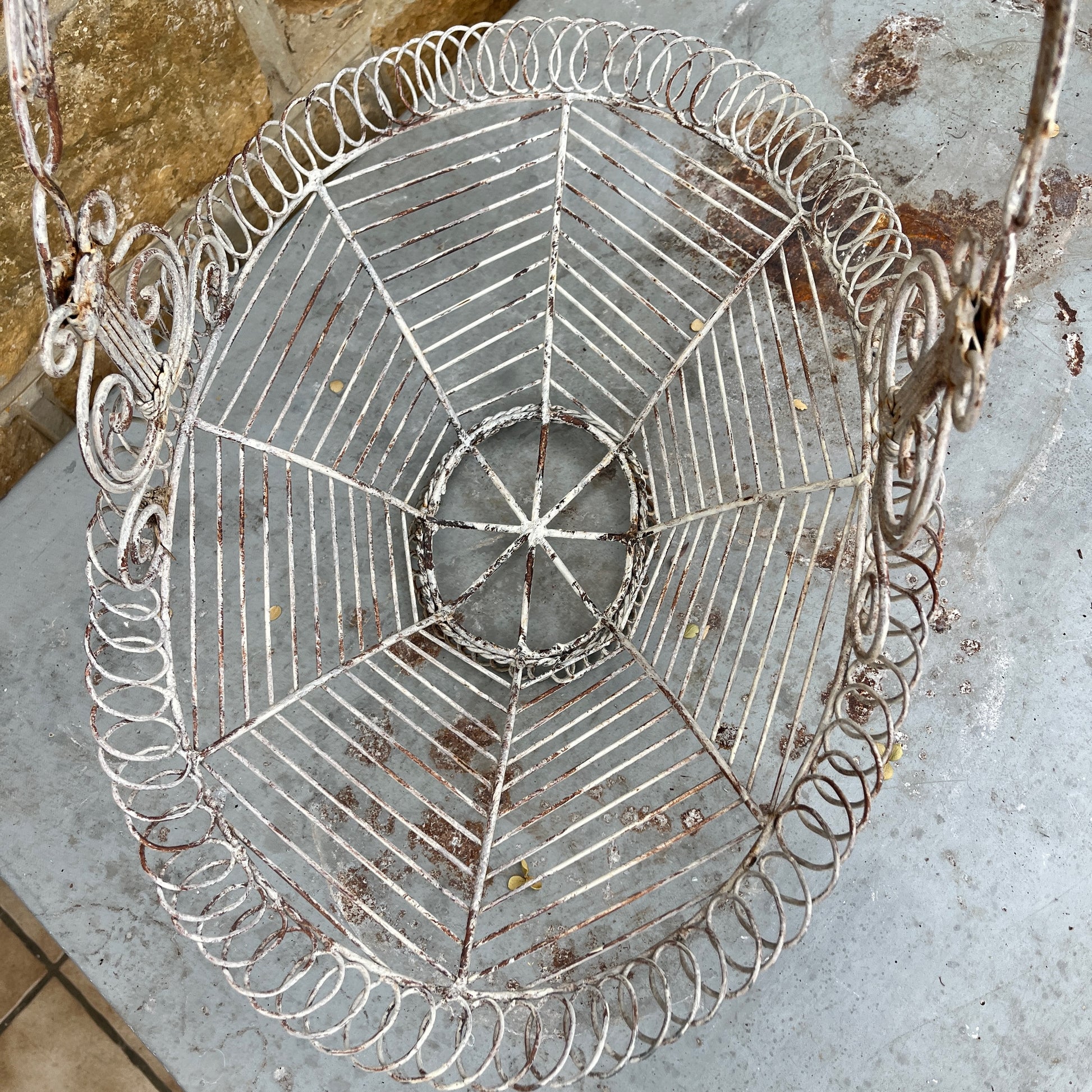 A French wire basket with a white, weathered finish, featuring an open, lattice-like design with delicate, curved edges. The basket includes one sturdy hinged handle, exuding rustic charm