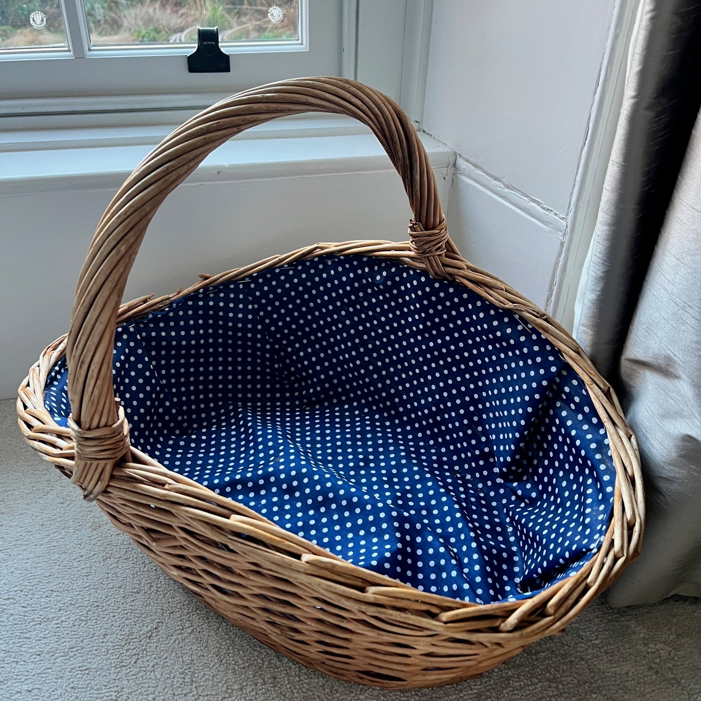 A large wicker basket with a charming blue polka dot fabric lining the interior, adding a playful touch to its rustic exterior