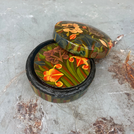 A set of round papier-mâché coasters, hand-painted with colorful floral designs in shades of yellow, red, blue and green, neatly stacked inside a matching rectangular papier-mâché box.