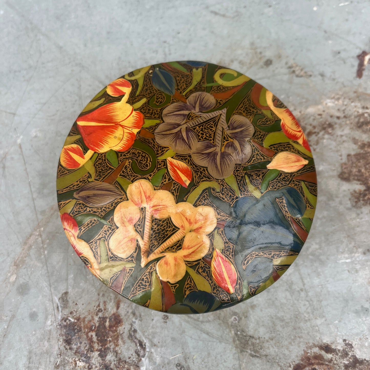 A set of round papier-mâché coasters, hand-painted with colorful floral designs in shades of yellow, red, blue and green, neatly stacked inside a matching rectangular papier-mâché box.