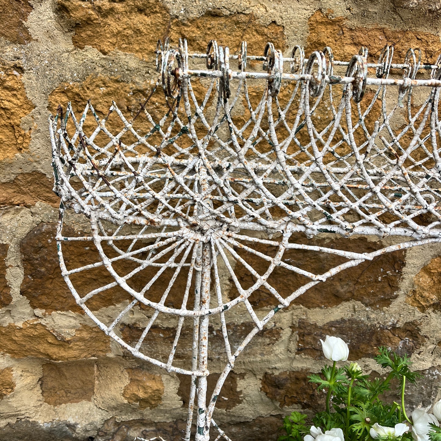 A Victorian decorative plant stand crafted from ornate wrought iron wire, featuring intricate scrollwork and floral patterns. The two-tiered stand, painted in a distressed white finish, supports small potted plants, exuding elegant vintage charm