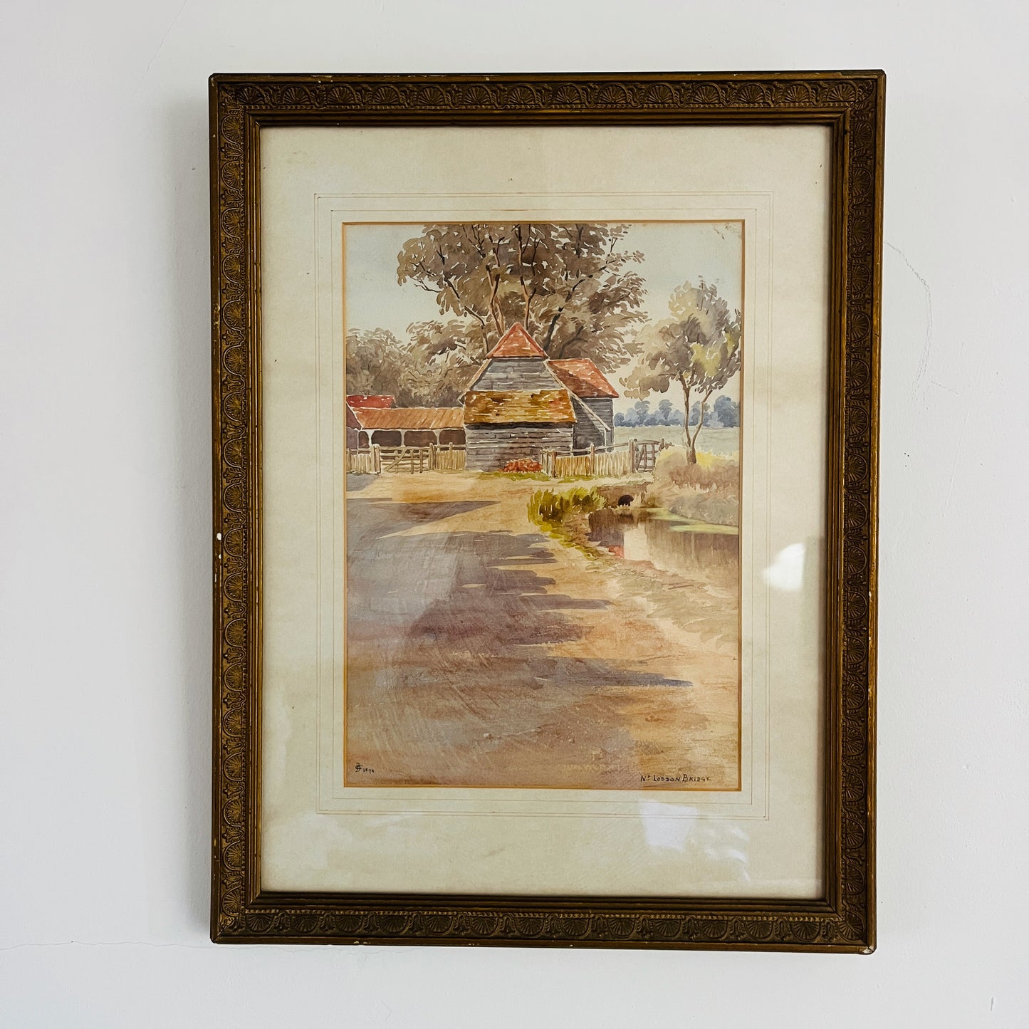 An antique watercolor painting of Loddon Bridge, depicting a serene riverside scene with a stone bridge arching over calm waters. The bridge features weathered stonework, flanked by lush greenery and trees in soft shades of green and brown.
Beside the bridge is an old farm building with a terracotta roof. The overall style is detailed yet gentle, characteristic of traditional watercolor techniques.
