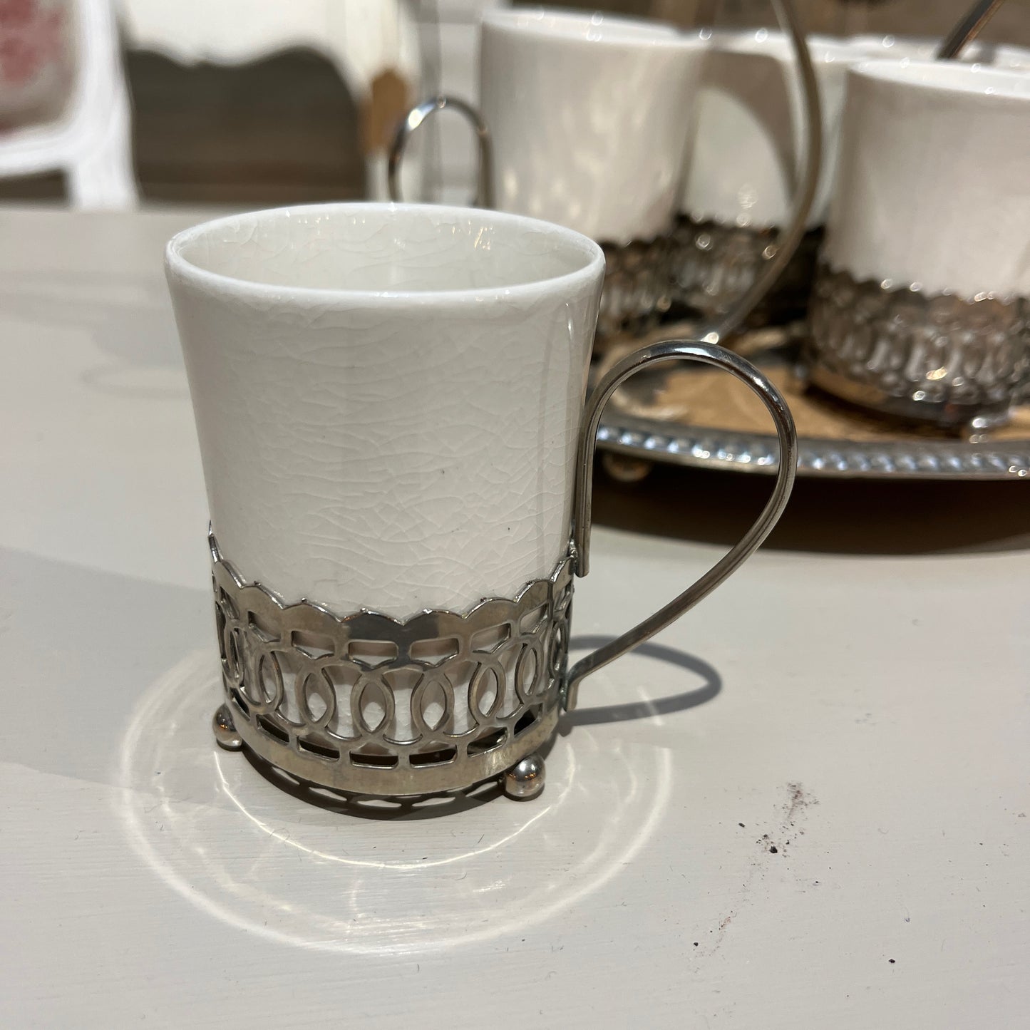 A set of six Wedgwood espresso cups, crafted from fine white china, neatly arranged inside a decorative metal case with a handle. The case rests on a tray, showcasing the cups' delicate design
