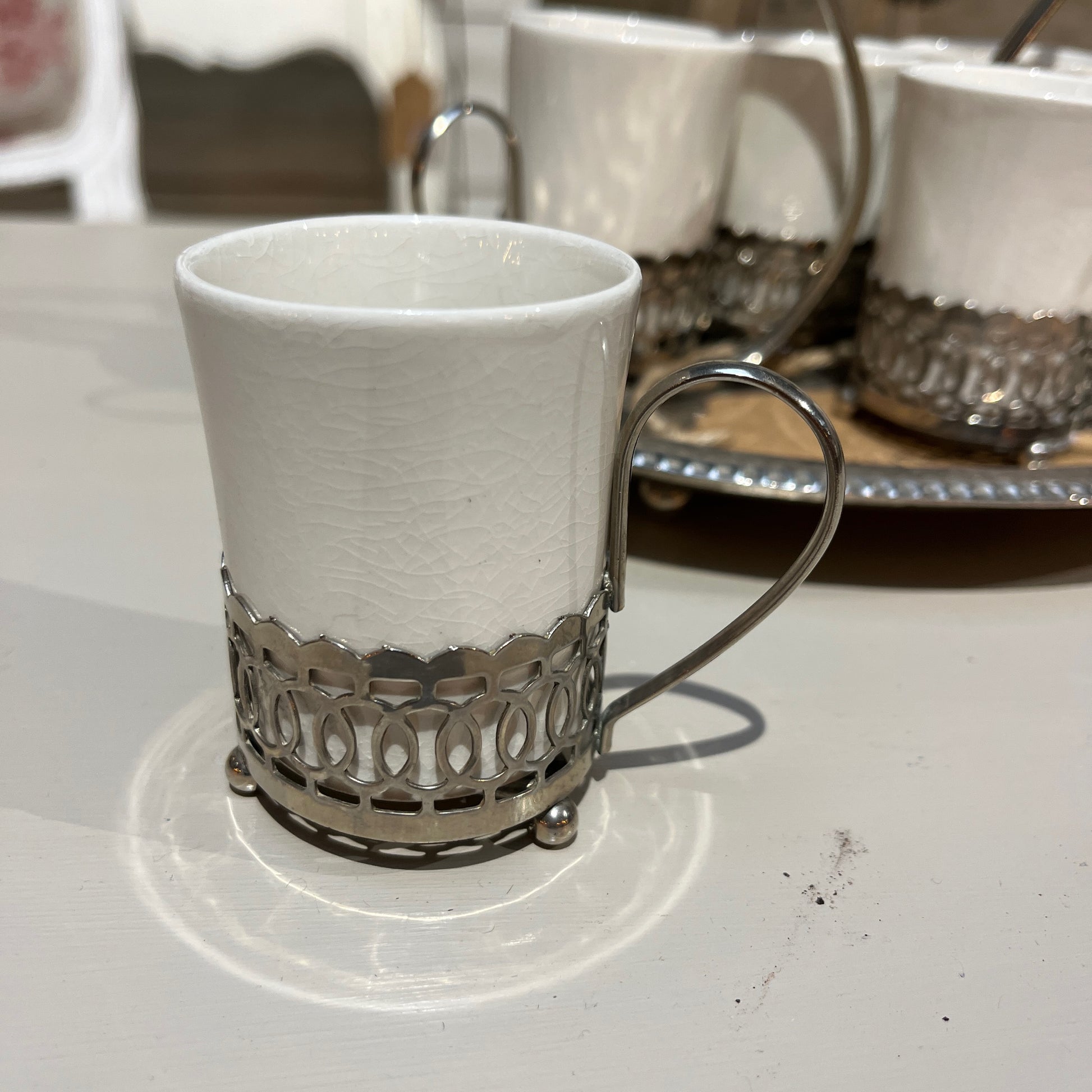 A set of six Wedgwood espresso cups, crafted from fine white china, neatly arranged inside a  decorative metal case with a handle. The case rests on a tray, showcasing the cups' delicate design
