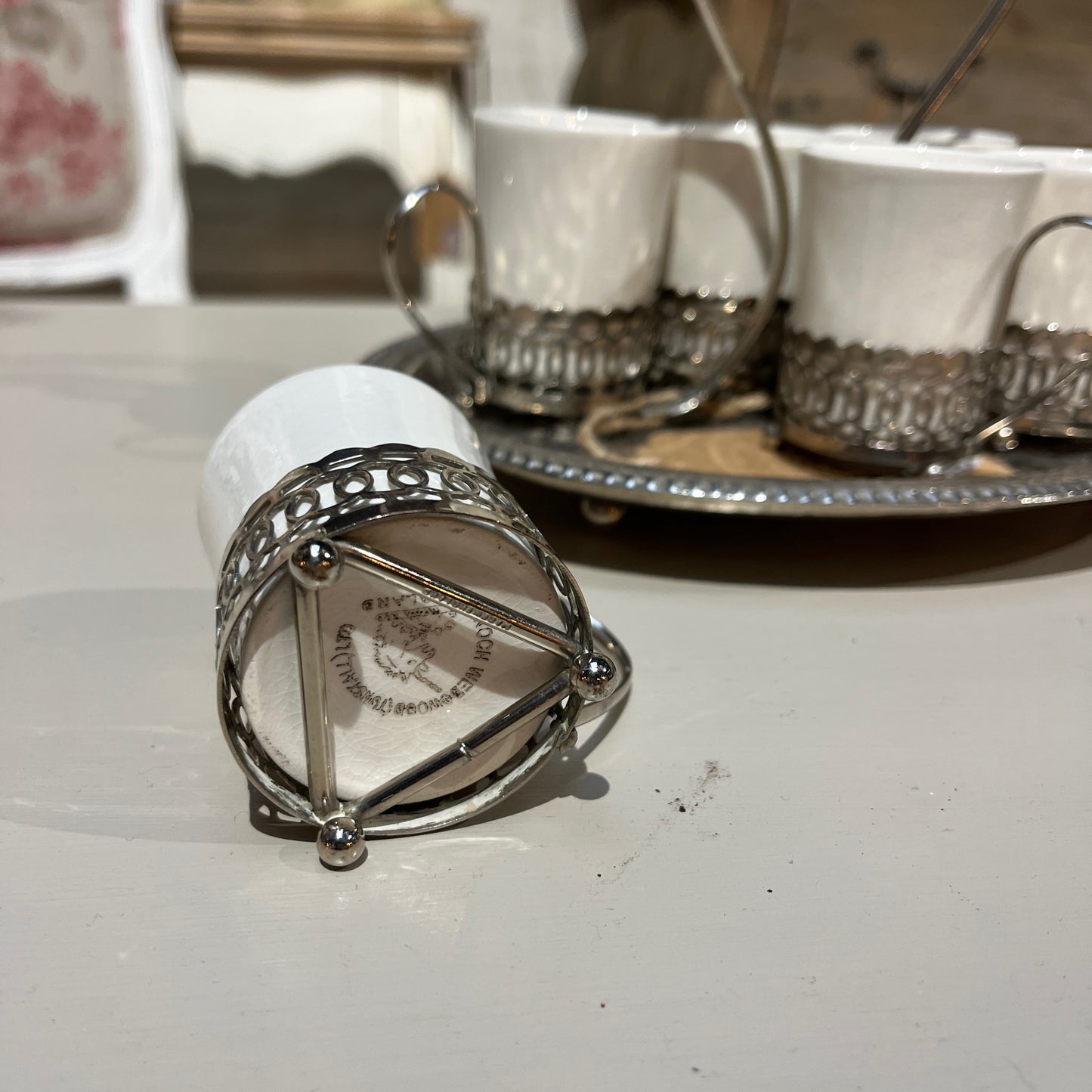 A set of six Wedgwood espresso cups, crafted from fine white china, neatly arranged inside a decorative metal case with a handle. The case rests on a tray, showcasing the cups' delicate design
