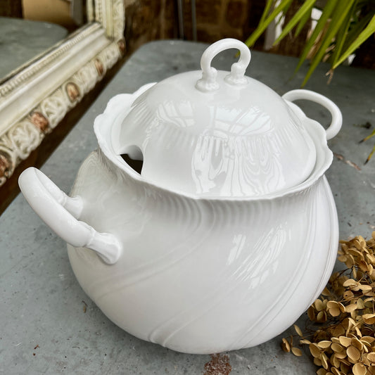 A round, white French-style casserole dish made of glazed ceramic, featuring a smooth, glossy finish. The dish has two small, curved handles on opposite sides and a fitted lid with a simple knob, exuding elegant, timeless charm