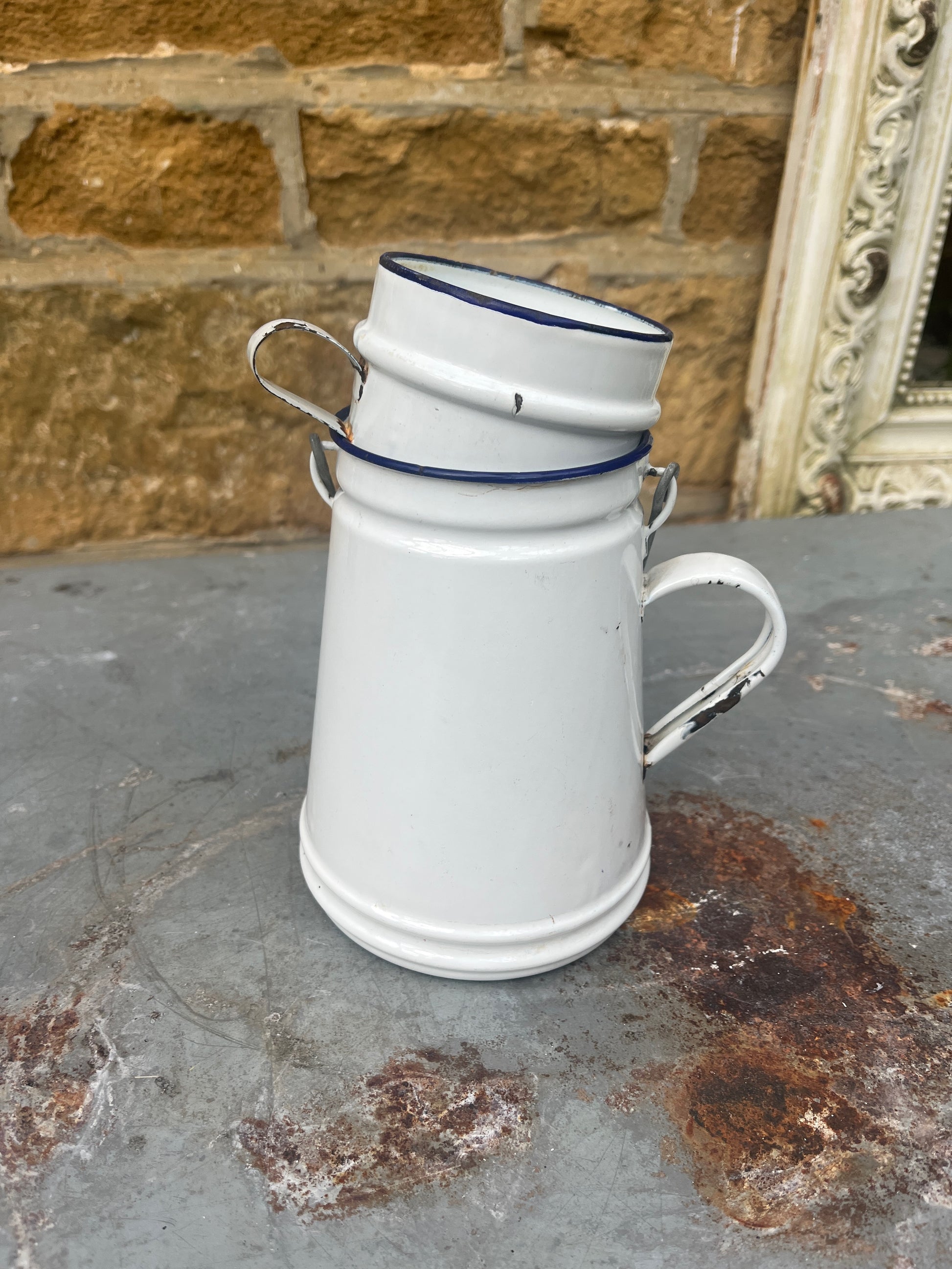 A small, vintage white billy can with a slightly weathered enamel finish, featuring a wire handle and a matching white enamel mug for a lid.