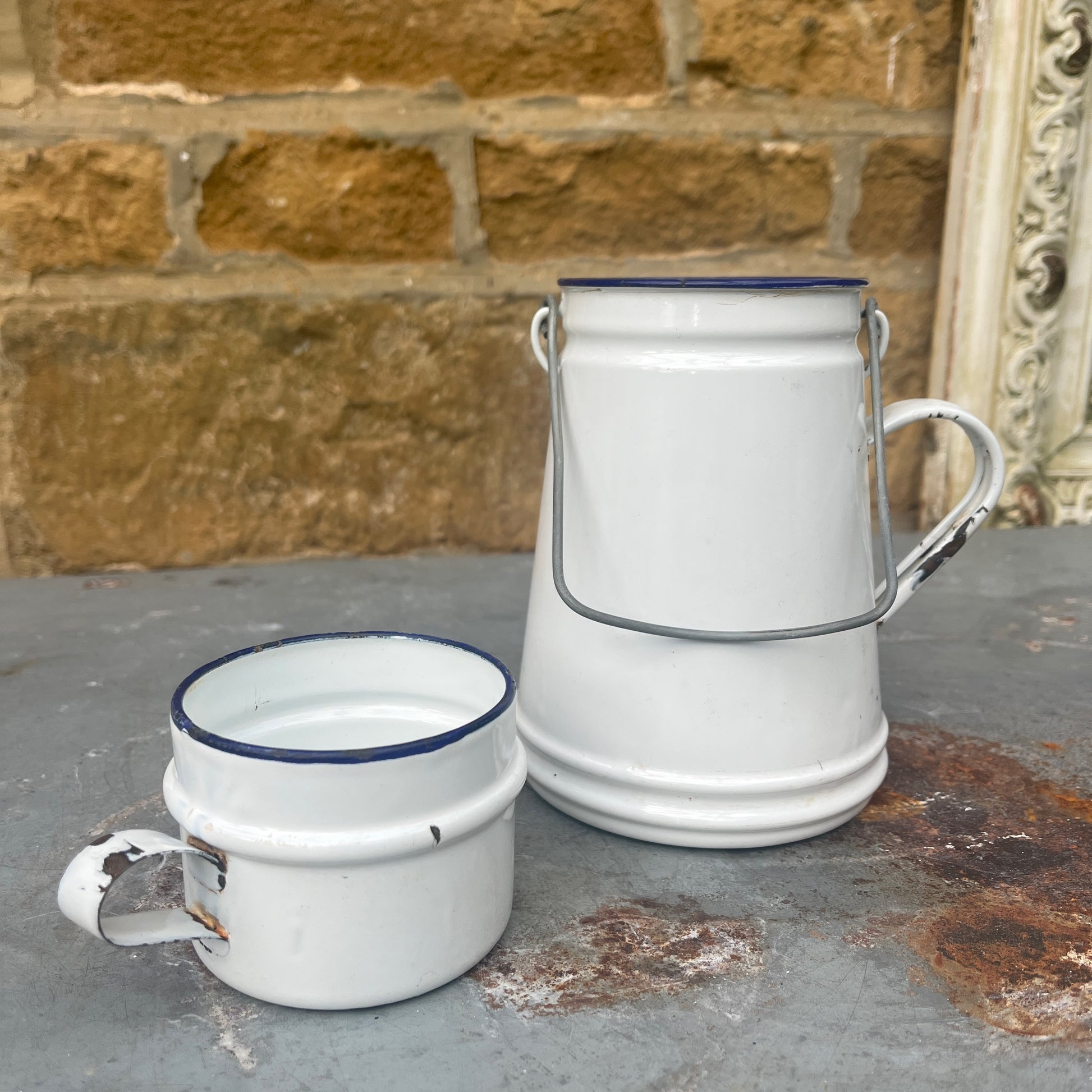 A small, vintage white billy can with a slightly weathered enamel finish, featuring a wire handle and a matching white enamel mug for a lid.
