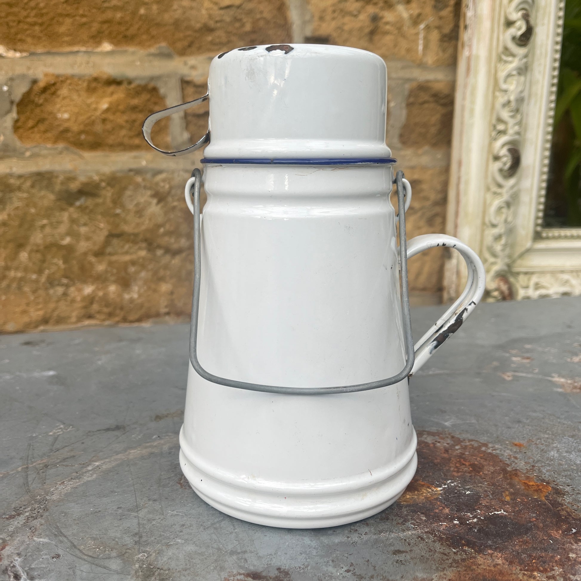A small, vintage white billy can with a slightly weathered enamel finish, featuring a wire handle and a matching white enamel mug for a lid.