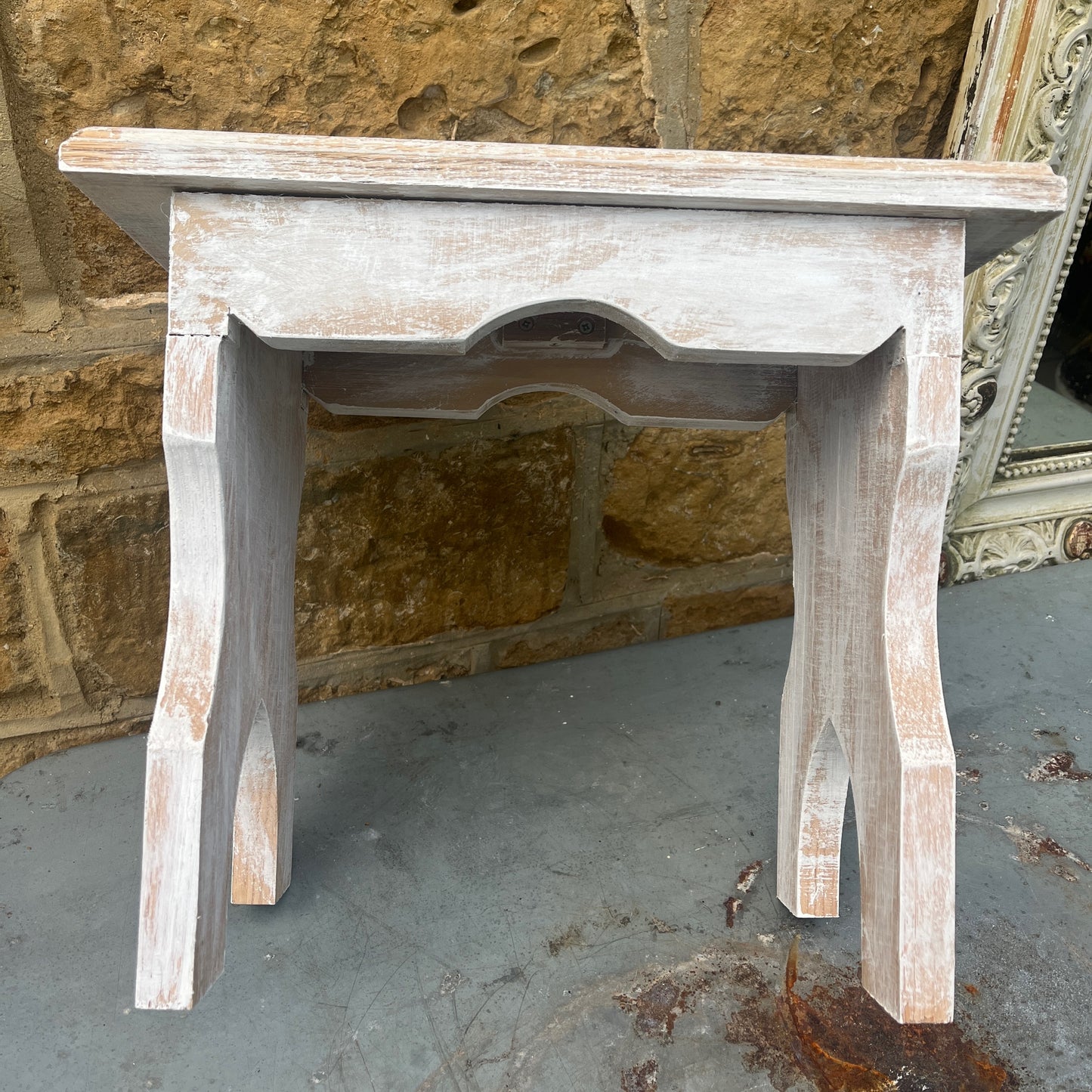 A vintage white wooden stool with a French design stencilled on the top, combining rustic appeal with elegant flair