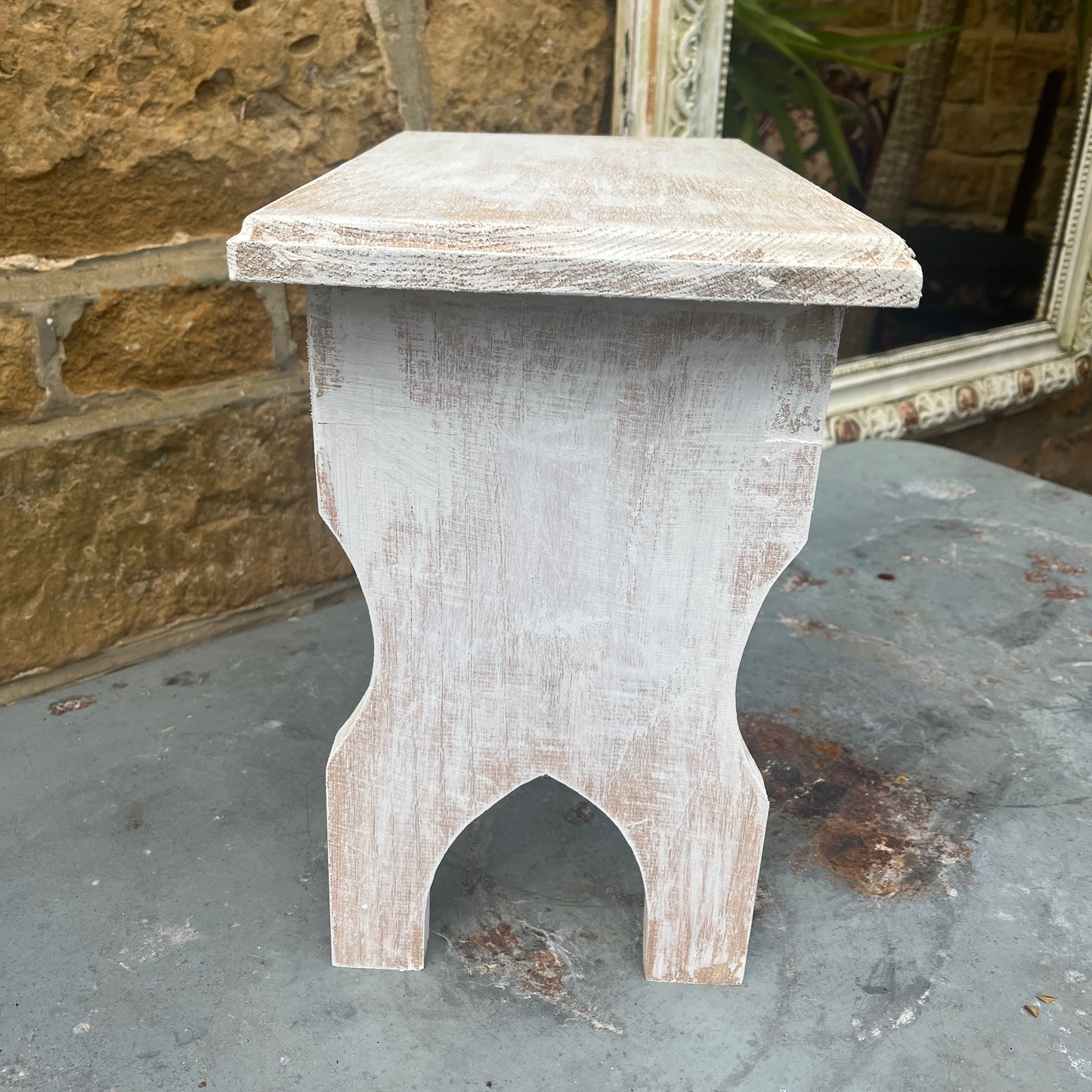 A vintage white wooden stool with a French design stencilled on the top, combining rustic appeal with elegant flair