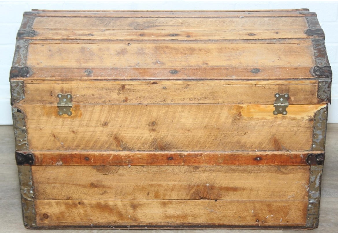 Antique steamer trunk with a sturdy rectangular form, metal hardware, and a weathered exterior showing age and travel wear.