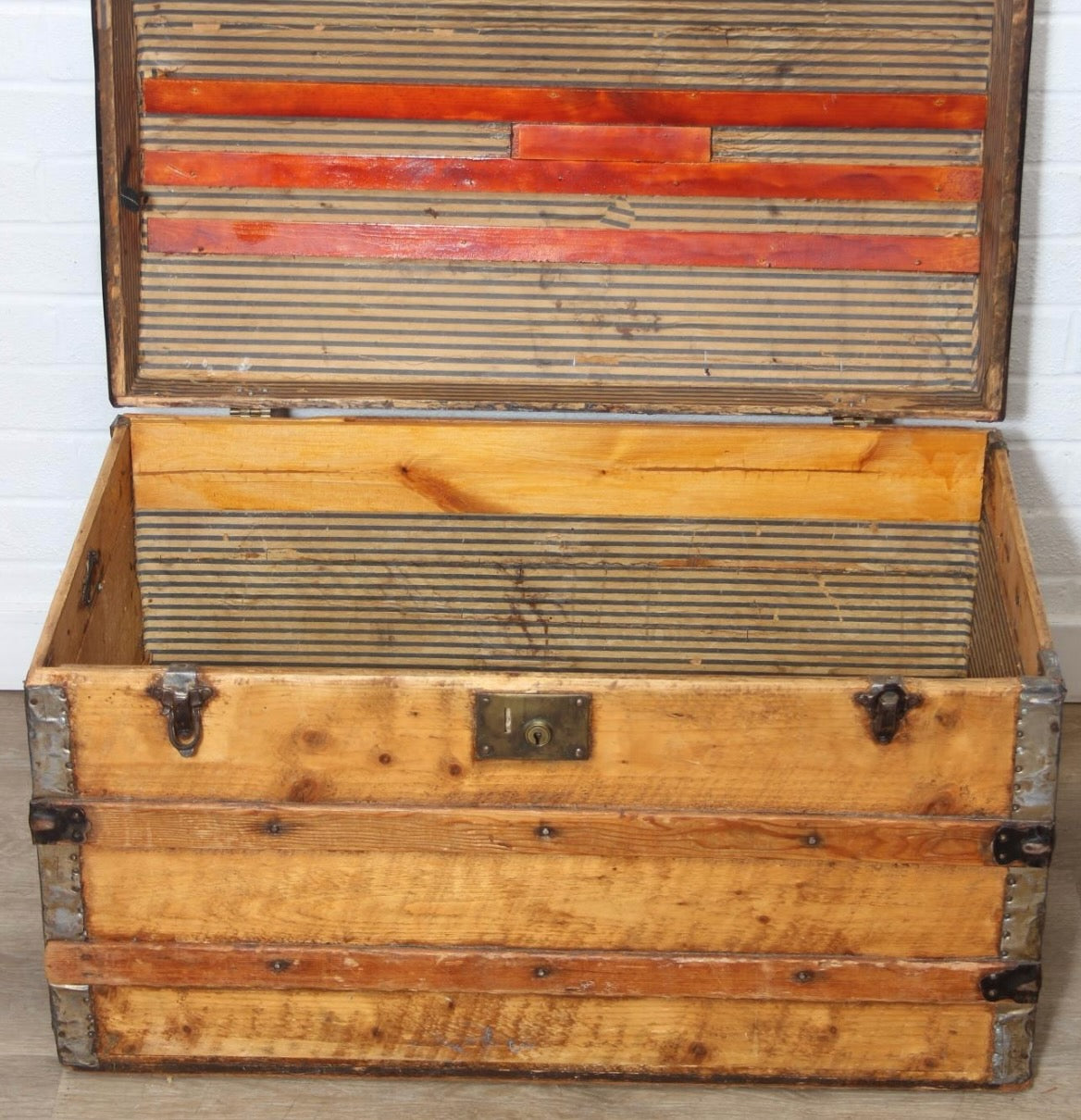 Antique steamer trunk with a sturdy rectangular form, metal hardware, and a weathered exterior showing age and travel wear.