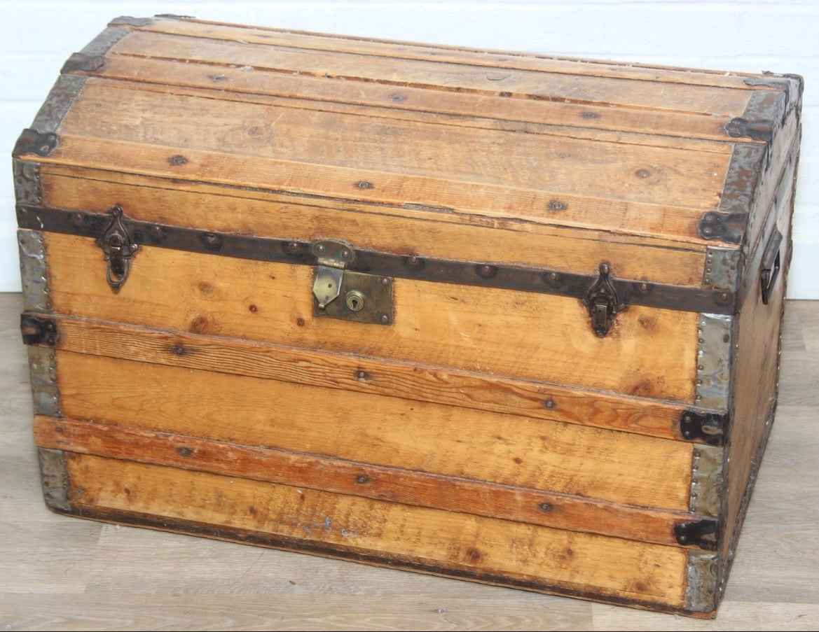 Antique steamer trunk with a sturdy rectangular form, metal hardware, and a weathered exterior showing age and travel wear.
