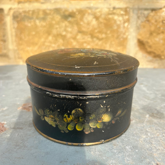 Vintage black round box with floral designs on a stone surface