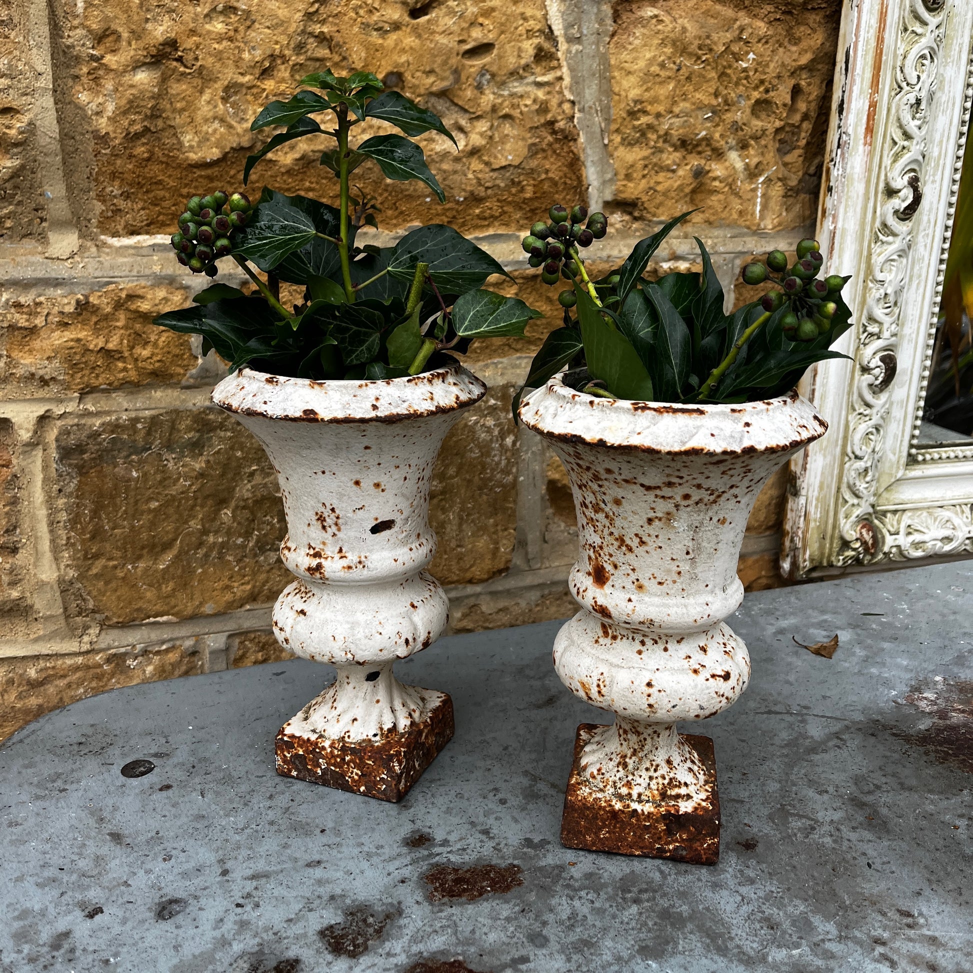 Pair of vintage Camana urns in a white finish. The urns feature classic shapes with decorative detailing and a weathered, aged patina, giving them a rustic, antique charm.