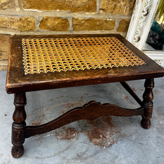 Antique low wooden stool featuring a woven cane top, curved rails and four turned legs with rounded feet.