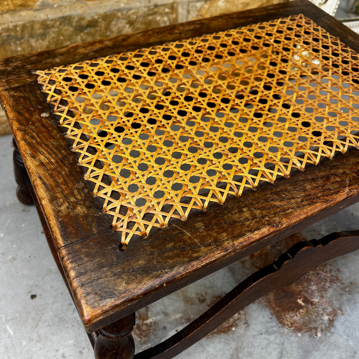 Antique low wooden stool featuring a woven cane top, curved rails and four turned legs with rounded feet.
