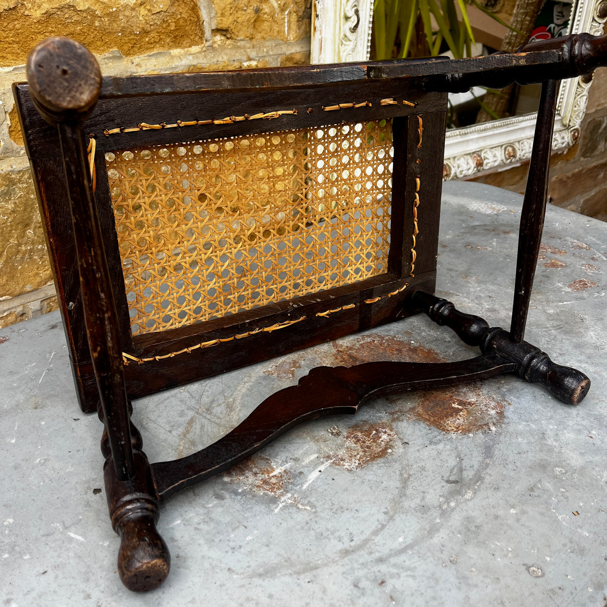 Antique low wooden stool featuring a woven cane top, curved rails and four turned legs with rounded feet.