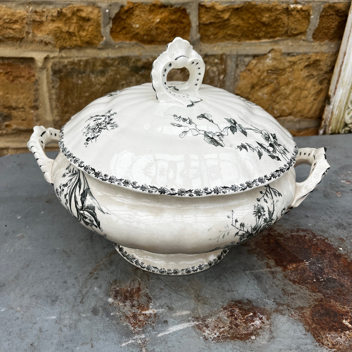 A white ceramic lidded tureen with dark green floral toile de Jouy patterns, on both the tureen and the lid.