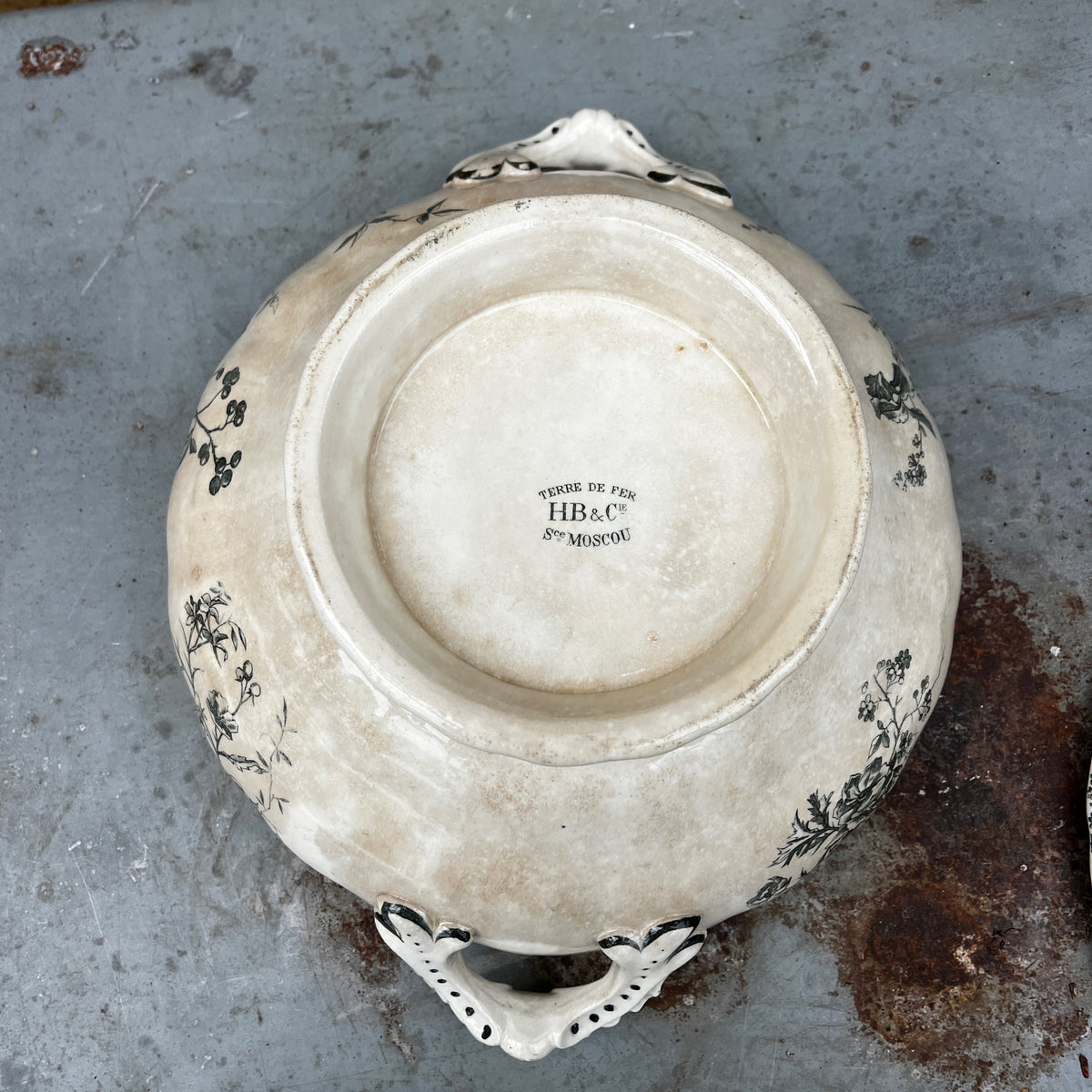 A white ceramic lidded tureen with dark green floral toile de Jouy patterns, on both the tureen and the lid.