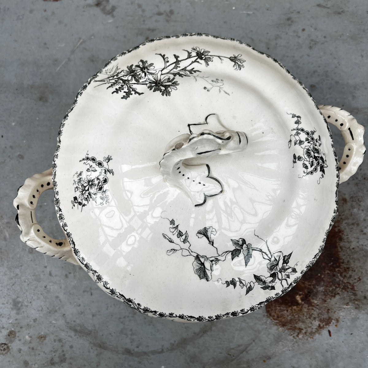 A white ceramic lidded tureen with dark green floral toile de Jouy patterns, on both the tureen and the lid.