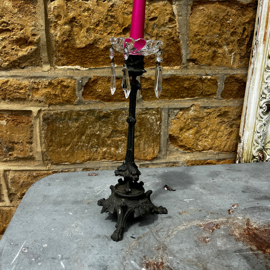 An ornate antique-style black metal candlestick with a decorative tripod base which iis topped with a clear glass bobeche adorned with hanging crystal prisms
