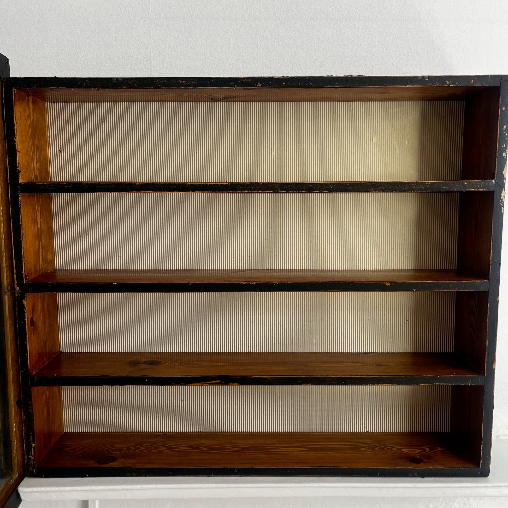 A stylish vintage glass display cabinet with a glass door stencilled with iconic designer names: Chanel, Christian Dior, Givenchy, and Gucci. The cabinet features wooden shelves which could be used to display luxury perfume bottles, fashion books and decorative objects.