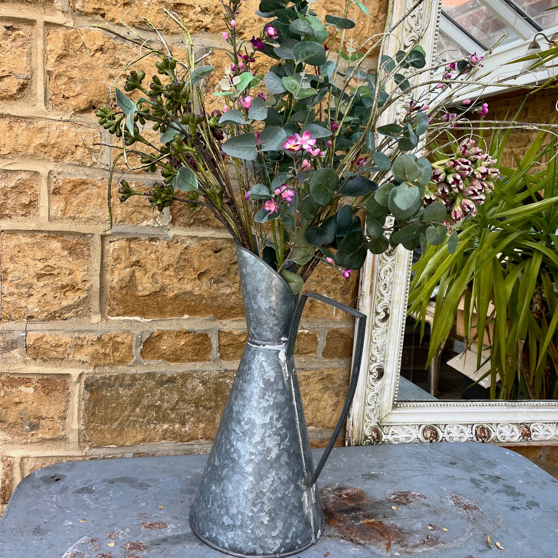 An elegant galvanized jug with a sleek, silver finish, featuring a stylized design with a gracefully curved handle and a flared spout