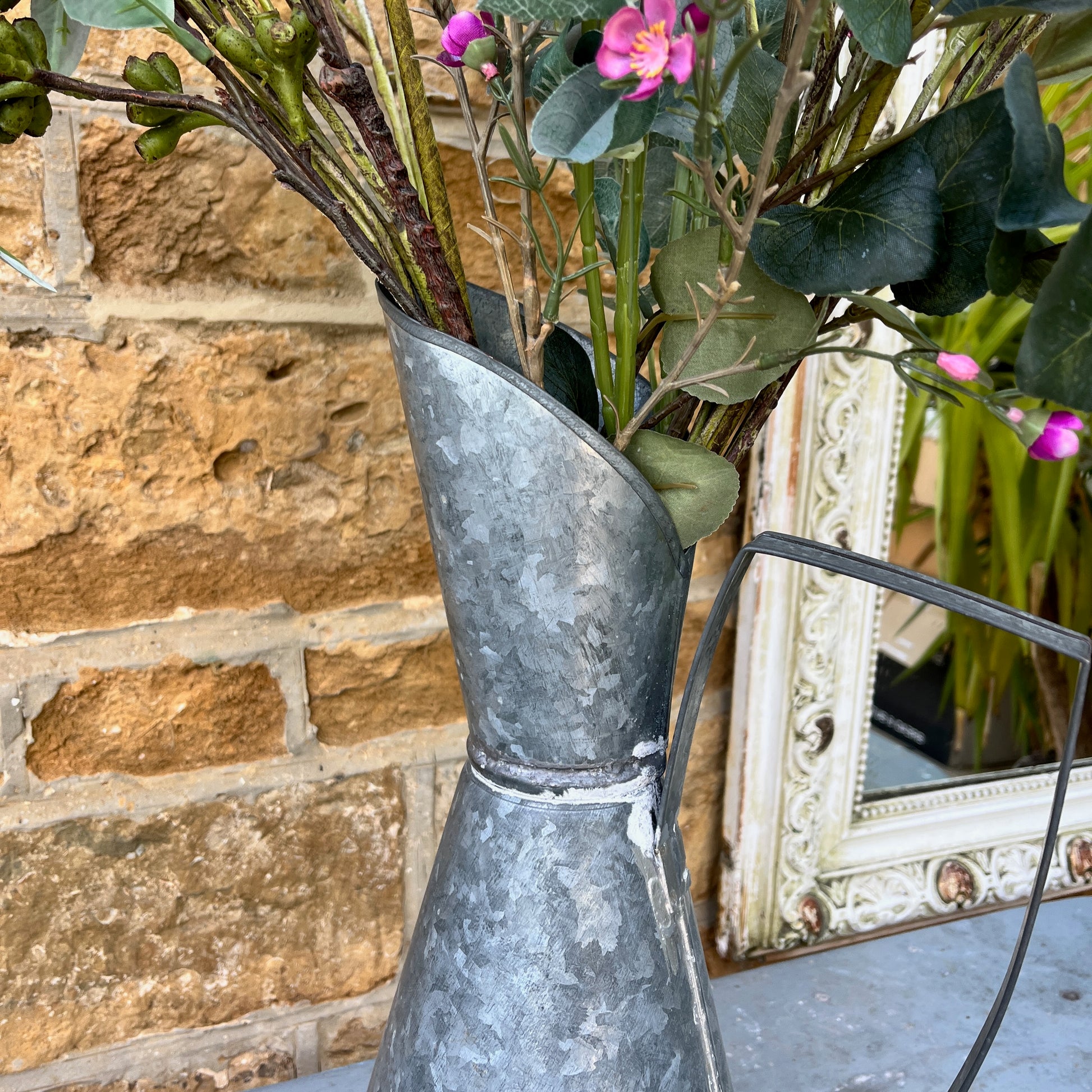 An elegant galvanized jug with a sleek, silver finish, featuring a stylized design with a gracefully curved handle and a flared spout