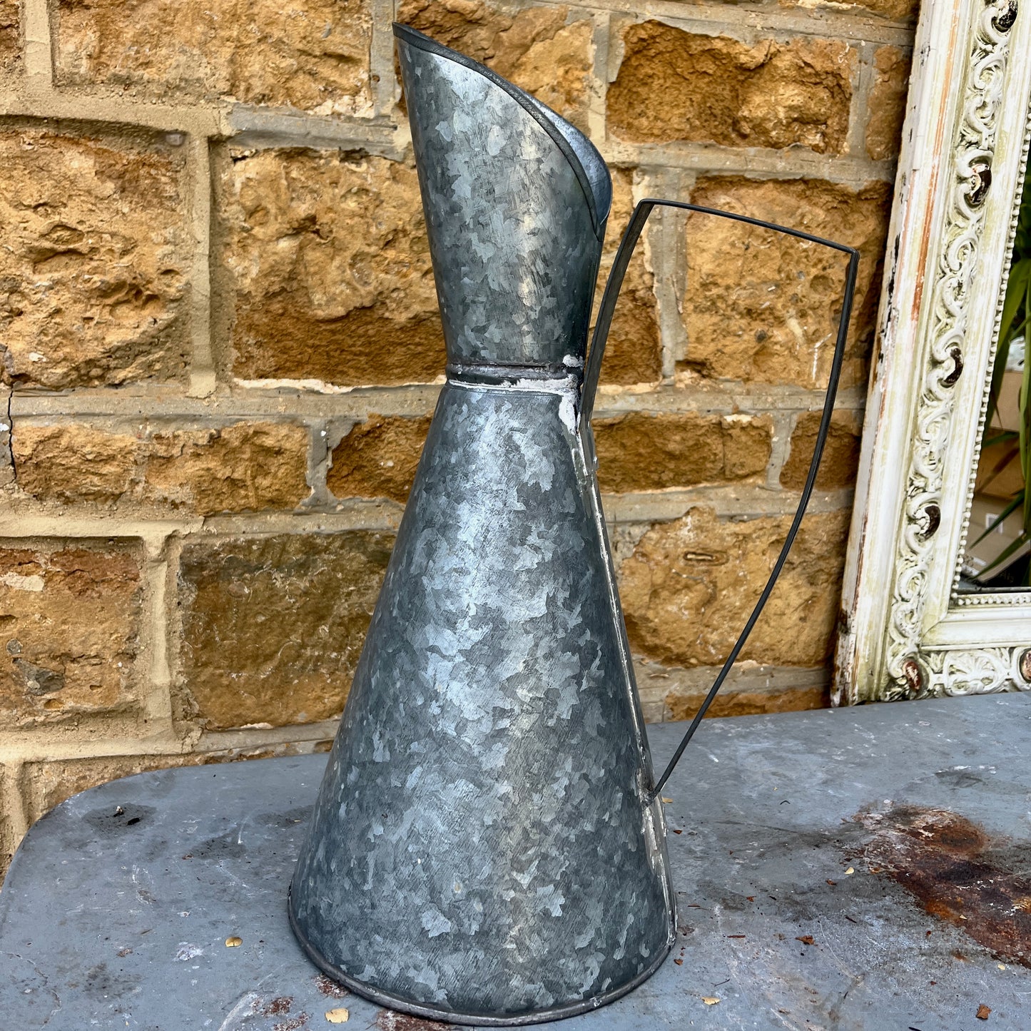 An elegant galvanized jug with a sleek, silver finish, featuring a stylized design with a gracefully curved handle and a flared spout