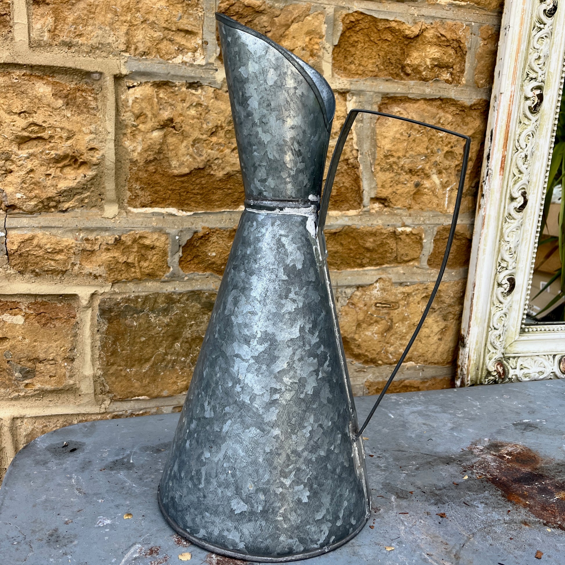 An elegant galvanized jug with a sleek, silver finish, featuring a stylized design with a gracefully curved handle and a flared spout